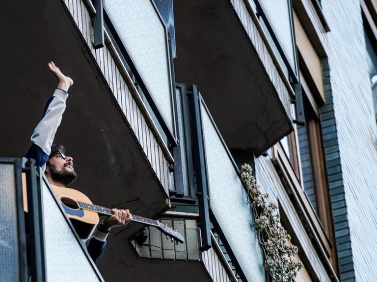 Ein Gitarrist steht auf einem Balkon in Mailand, Italien, und spielt für seine Nachbarschaft.