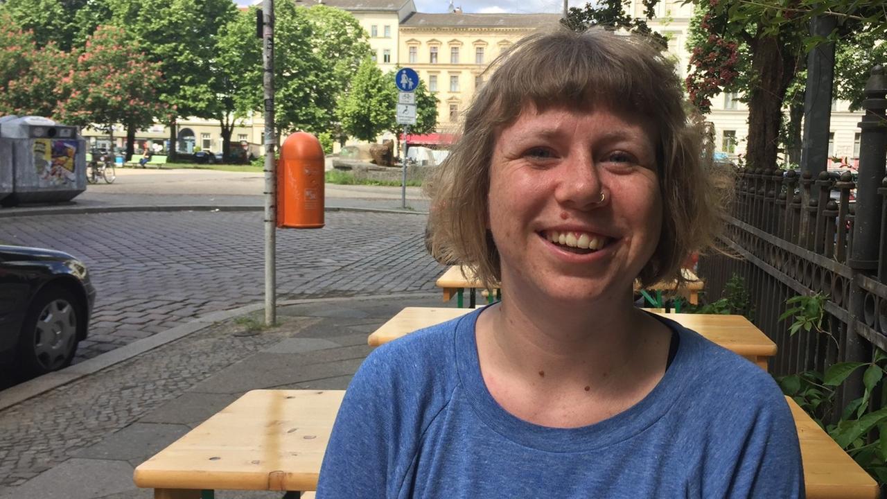 Susanna Raab von der Initiative "Deutsche Wohnen & Co. enteignen" sitzt an einem Tisch auf einer Berliner Straße.