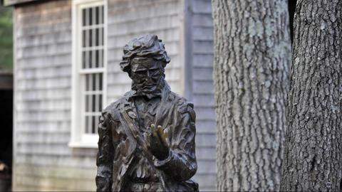 Statue von Henry David Thoreau vor der nachgebauten Hütte und Bäumen