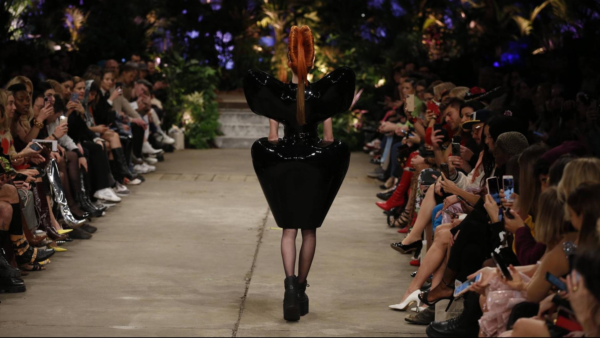 Eine Frau in einem extravaganten schwarzen Kleid in einer Rückenansicht auf dem Laufsteg.