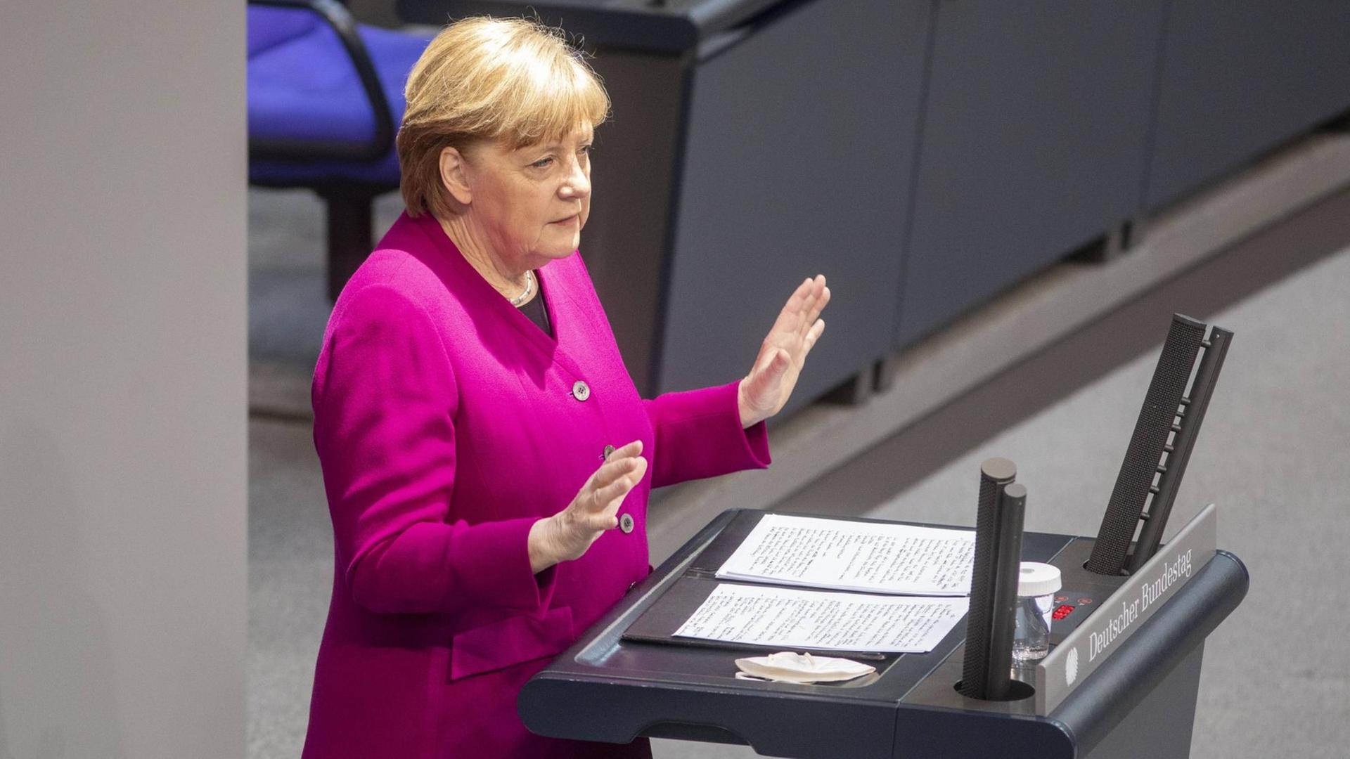 Angela Merkel steht am Rednerpult im Bundestag und spricht, beide Hände leicht erhoben