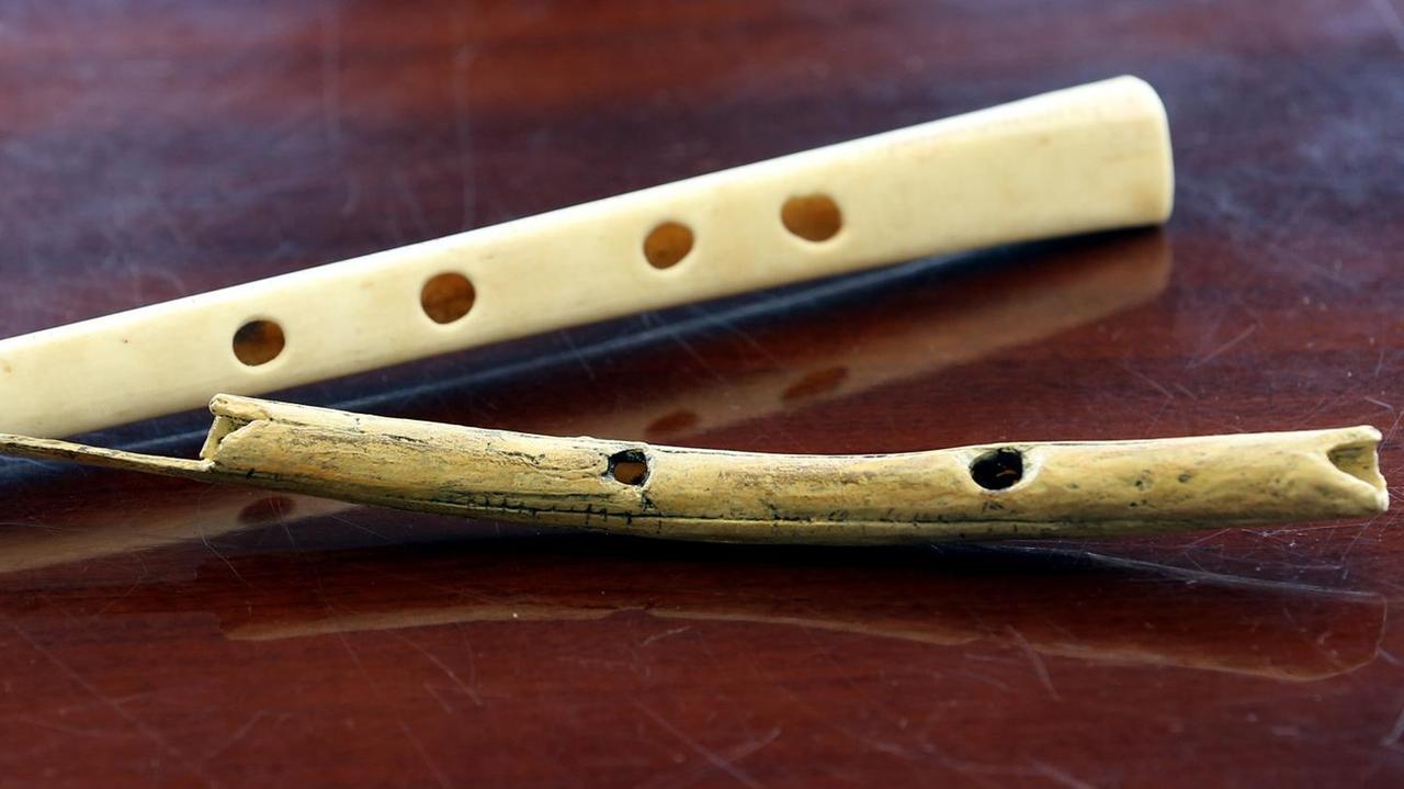 Der Nachbau einer 38000 Jahre alten Flöte aus Geierflügelknochen (oben) und eine Flöte aus Mammutelfenbein liegen nebeneinander auf einem dunklen Holztisch.