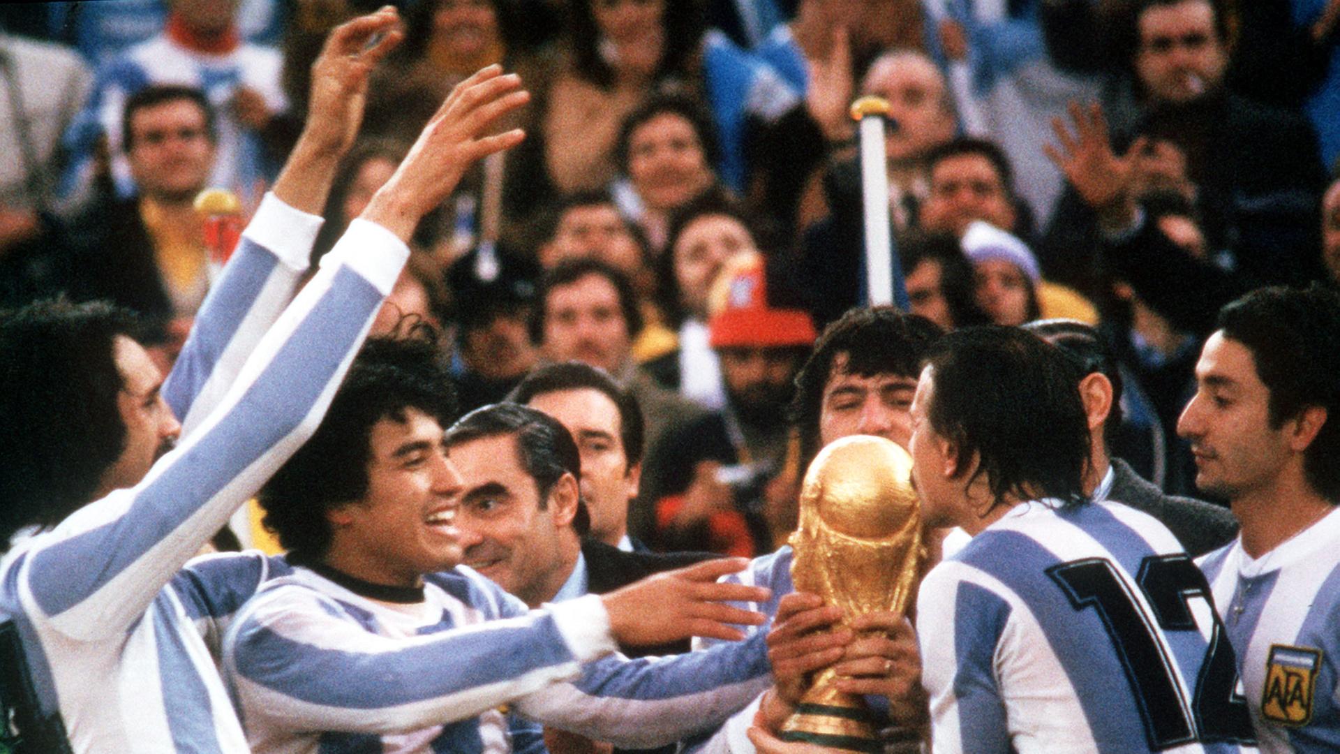 Fünf argentinische Nationalspieler im Sportdress halten den Weltmeisterpokal, küssen ihn und jubeln.