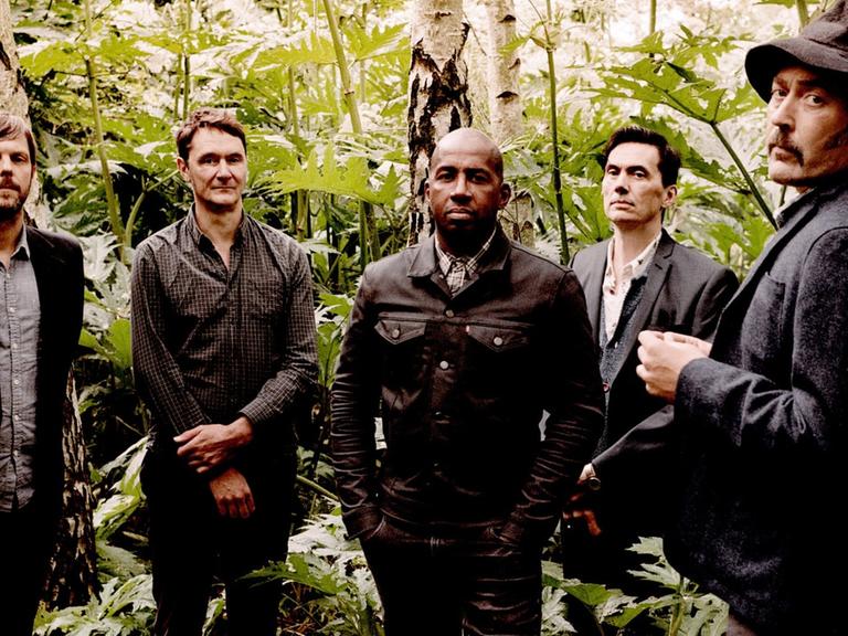 Fünf Männer stehen in einem Waldstück und blicken in die Kamera.