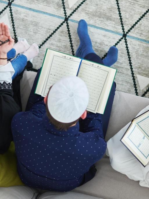 Blick von oben auf eine junge muslimische Familie, die während des Ramadan im Koran lesen. (Symbolbild)