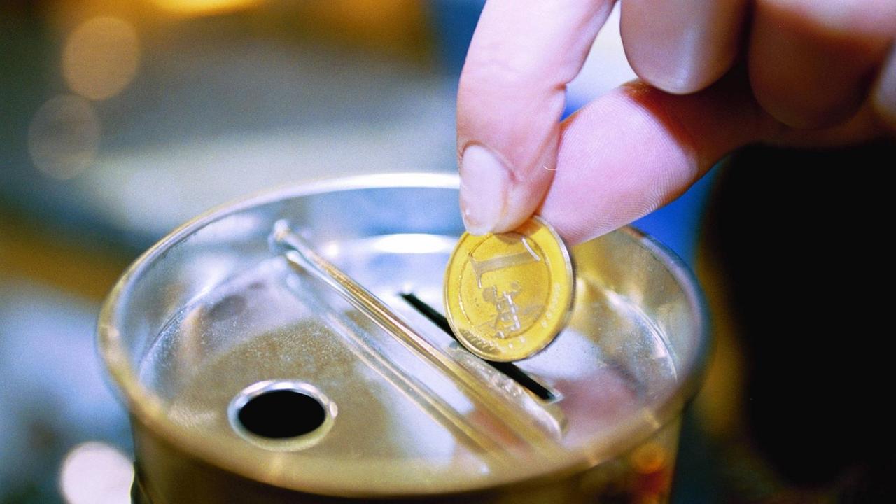 Eine Euromünze wird in eine Sammelbüchse gesteckt.