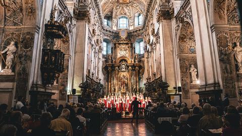 In einem großen, barocken Kirchenraum steht der rot gekleidete Chor im Altarraum.