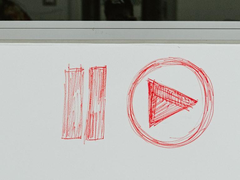 Das Logo für "Play Pause /Abspielen anhalten" ist mit rotem Stift auf einen hellgrauen Hintergrung gezeichnet.