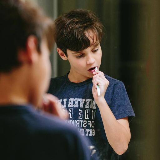 Ein Junge steht vor dem Spiegel und putzt sich die Zähne. Zu sehen sind sein Rücken und im Spiegel seine Reflexion.