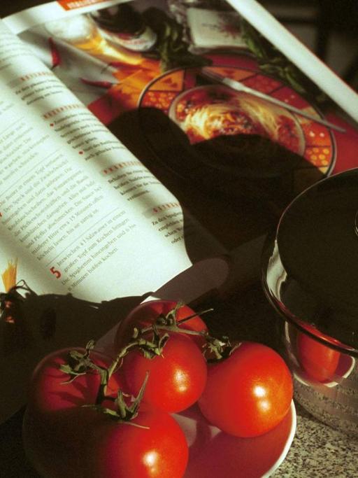 Tomaten, ein Kochbuch und ein Topf stehen bereit, um Spaghetti zu kochen.