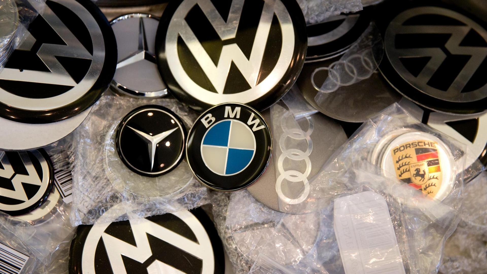 Die Logos verschiedener Auto-Marken liegen durcheinander auf einem Tisch.