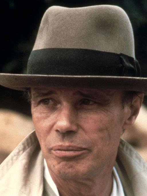 Porträt von Joseph Beuys mit Hut und hochgeschlagenem Kragen eines Mantels.