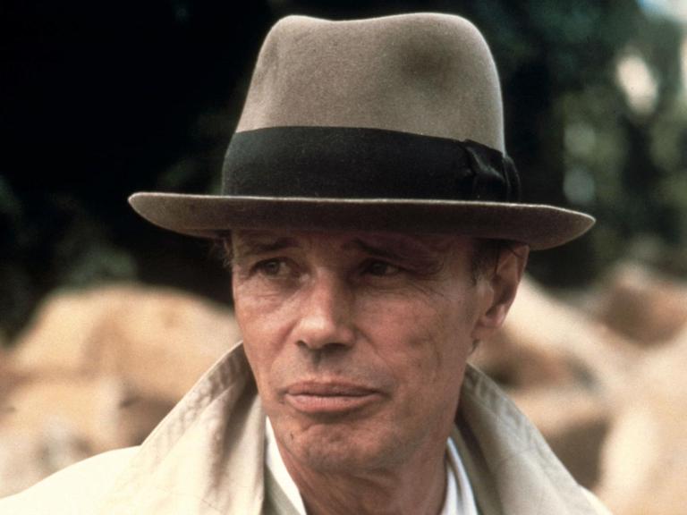 Porträt von Joseph Beuys mit Hut und hochgeschlagenem Kragen eines Mantels.