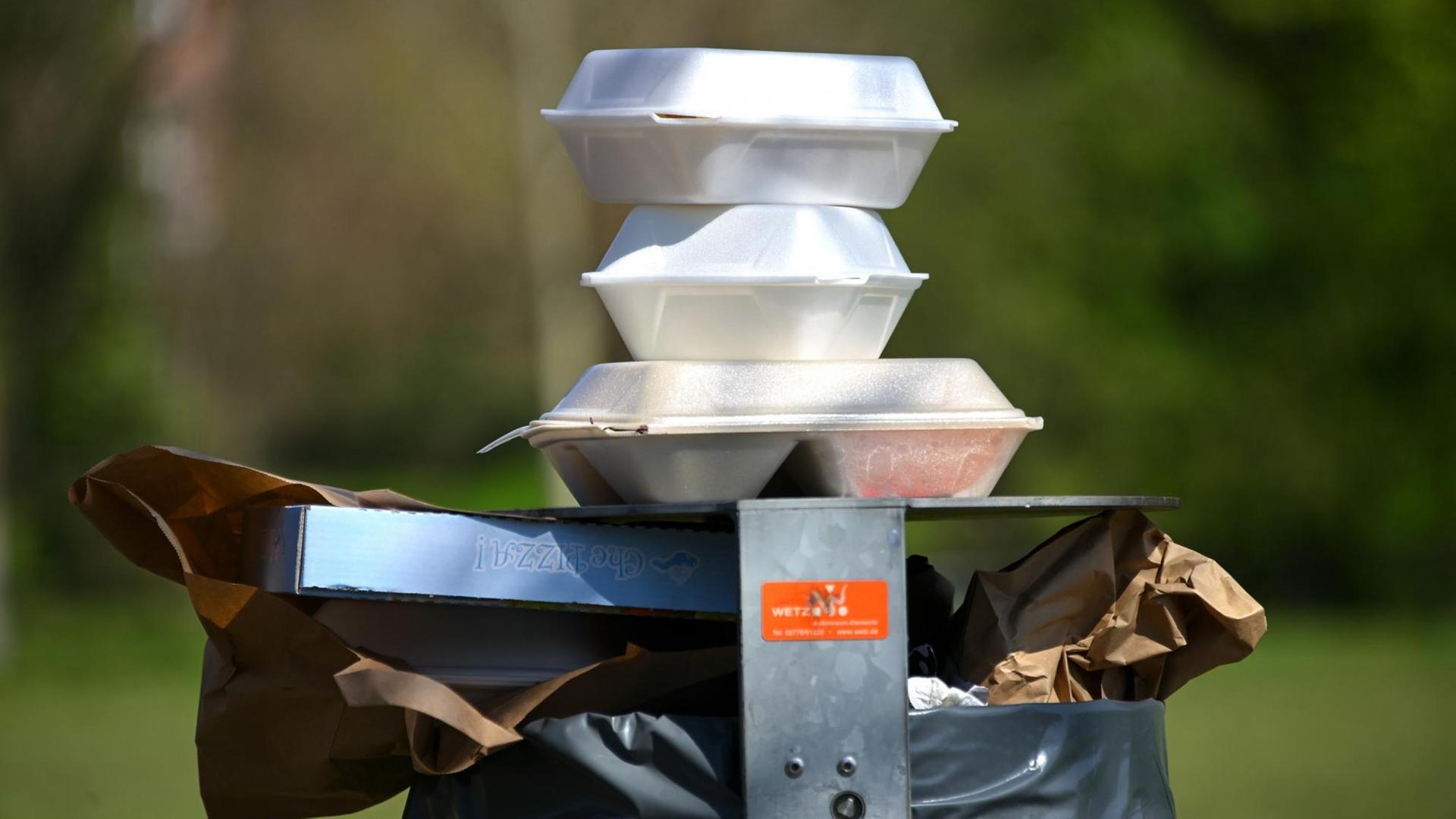 Leere Speise-Verpackungen stapeln sich im Nordstadtpark in Kassel auf einem Mülleimer.