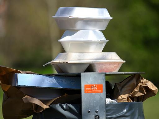 Leere Speise-Verpackungen stapeln sich im Nordstadtpark in Kassel auf einem Mülleimer.