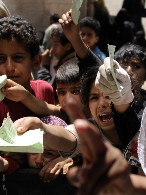 Kinder in Sanaa im Jemen strecken Zetteln in ihren Händen aus und rufen.
