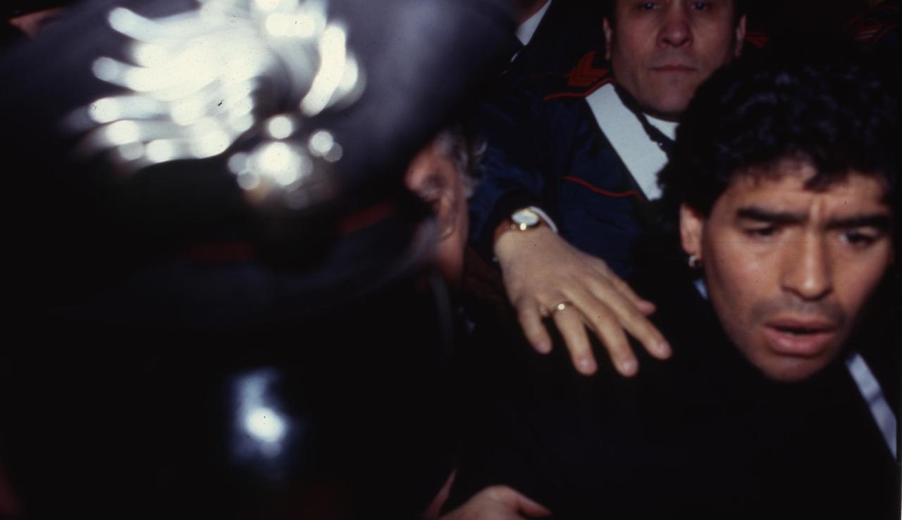 Diego Maradona verlässt das Tribunal von Neapel 1991. Er wird von Security begleitet und drängt sich durch ein Blitzlichtgewitter.