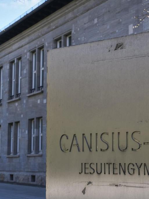 Das Canisius-Kolleg in Berlin-Tiergarten. Ein graues Schulgebäude, davor ist eine Tafel mit dem Namen der Schule.