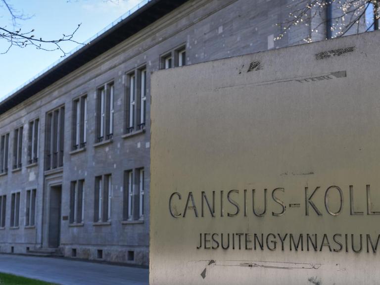 Das Canisius-Kolleg in Berlin-Tiergarten. Ein graues Schulgebäude, davor ist eine Tafel mit dem Namen der Schule.