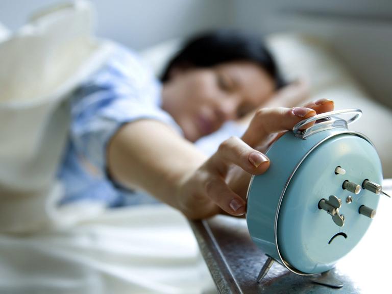 Eine junge Frau liegt im Bett und schaltet einen Wecker aus.