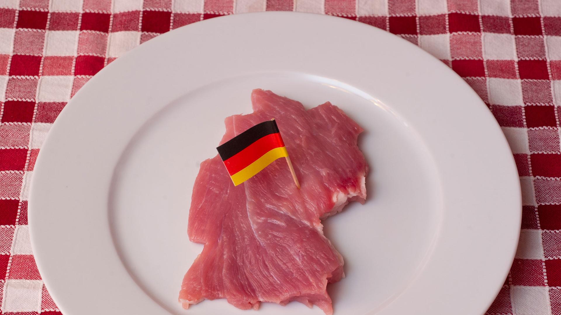 Ein Stück Schweinefleisch, geschnitten wie der Umriss von Deutschland und mit einer kleinen Deutschlandfahne