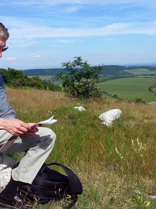 Der Komponist Hauke Harder sitzt in einer weiten Hügellandschaft auf einem Stein