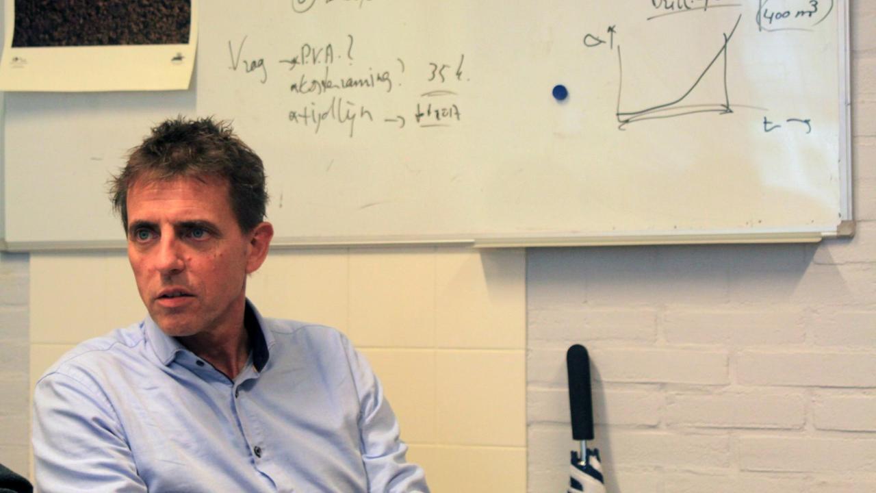 Henk Jonkers sitzt vor einer beschrifteten Tafel in einem Seminarraum