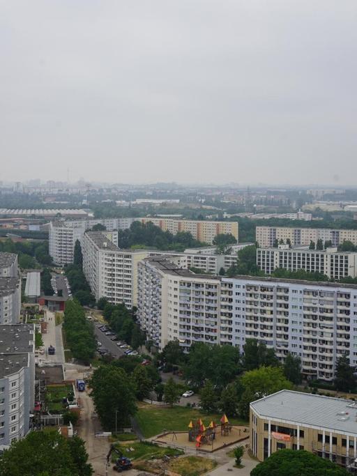 Ein Blick von einer erhöhten Perspektive auf die zahlreichen Hochhaussiedlungen des Berliner Bezirks Marzahn. Zwischen den Gebäuden sind zahlreiche Bäume zu sehen. Der Himmel ist grau.