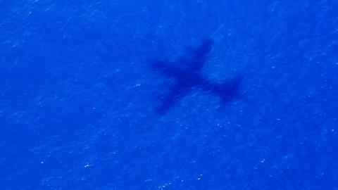 Man sieht den Schatten eines großen Flugzeuges über dem Meer