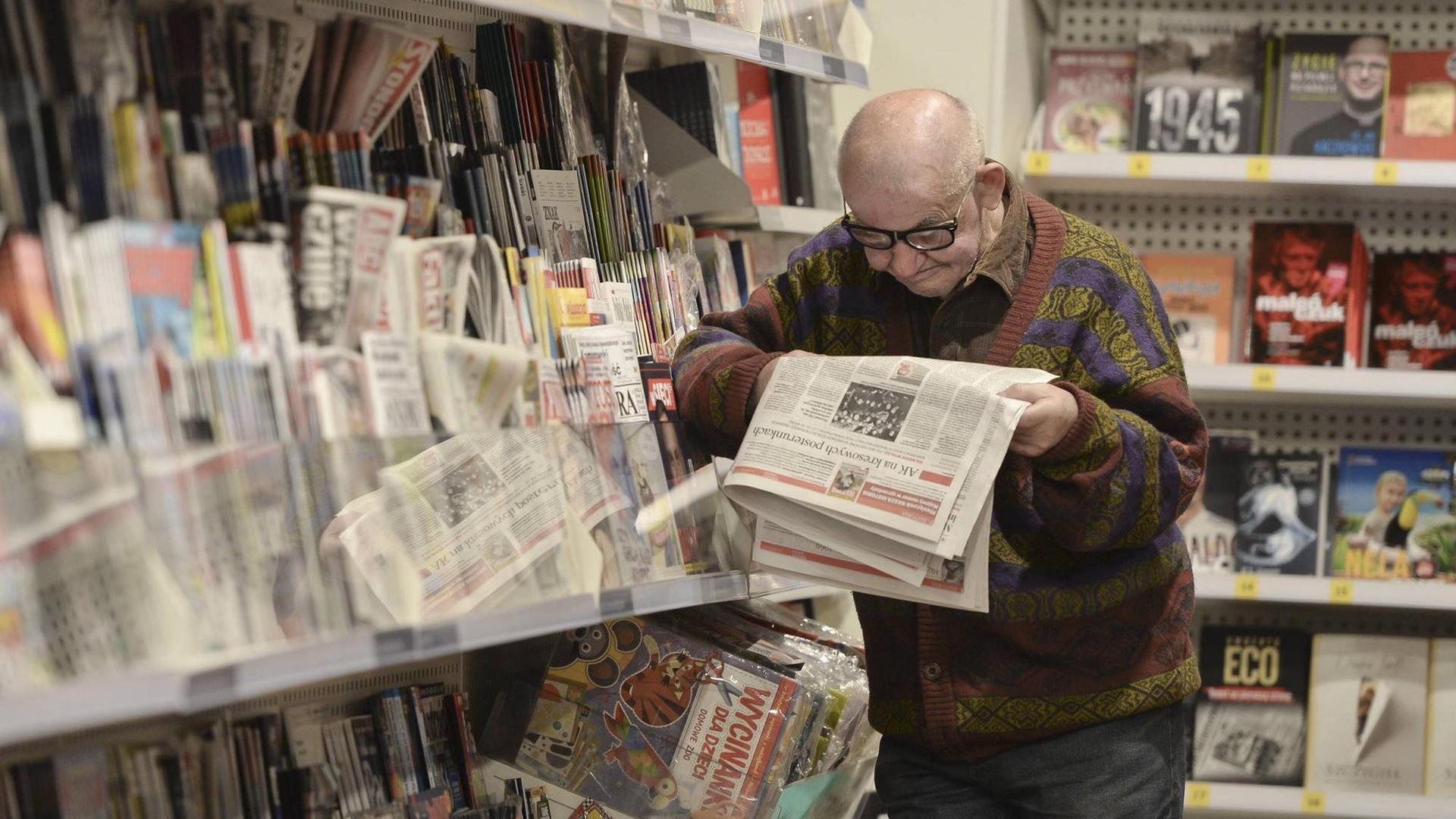 Mann lehnt an Zeitungsregal und liest in einer Zeitung 