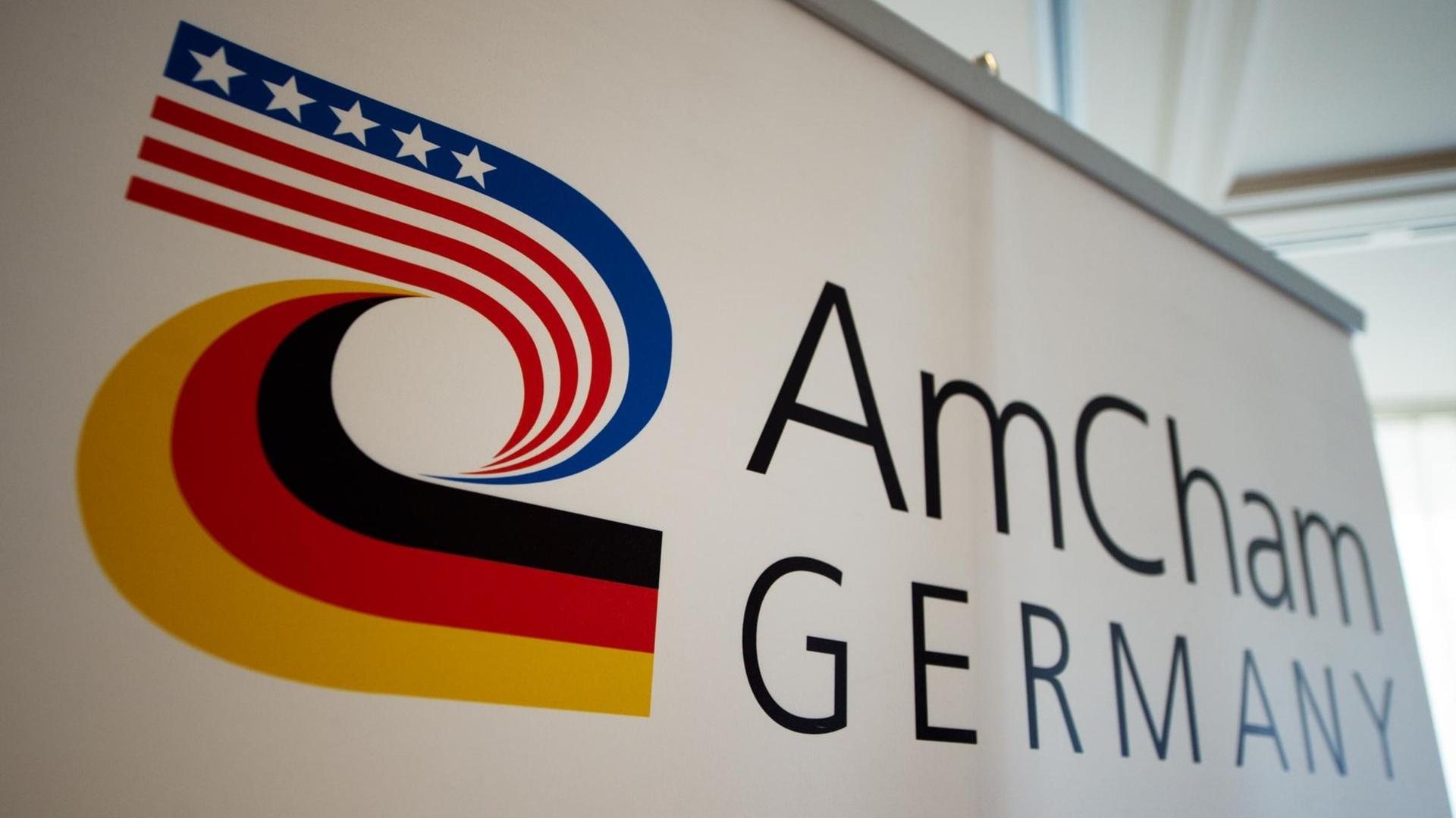 Auf einer Fotowand ist das Logo der Amerikanischen Handelskammer in Deutschland, der AmCham Germany, im Hotel "Hilton Park" in München (Bayern) zu sehen.