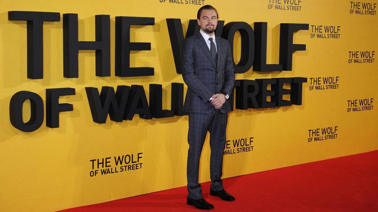 Sie sehen Leonardo Di Caprio bei der Filmpremiere von 'The Wolf of Wall Street' in London. Er steht vor einer gelben Wand mit dem Filmtitel in schwarzen Buchstaben.