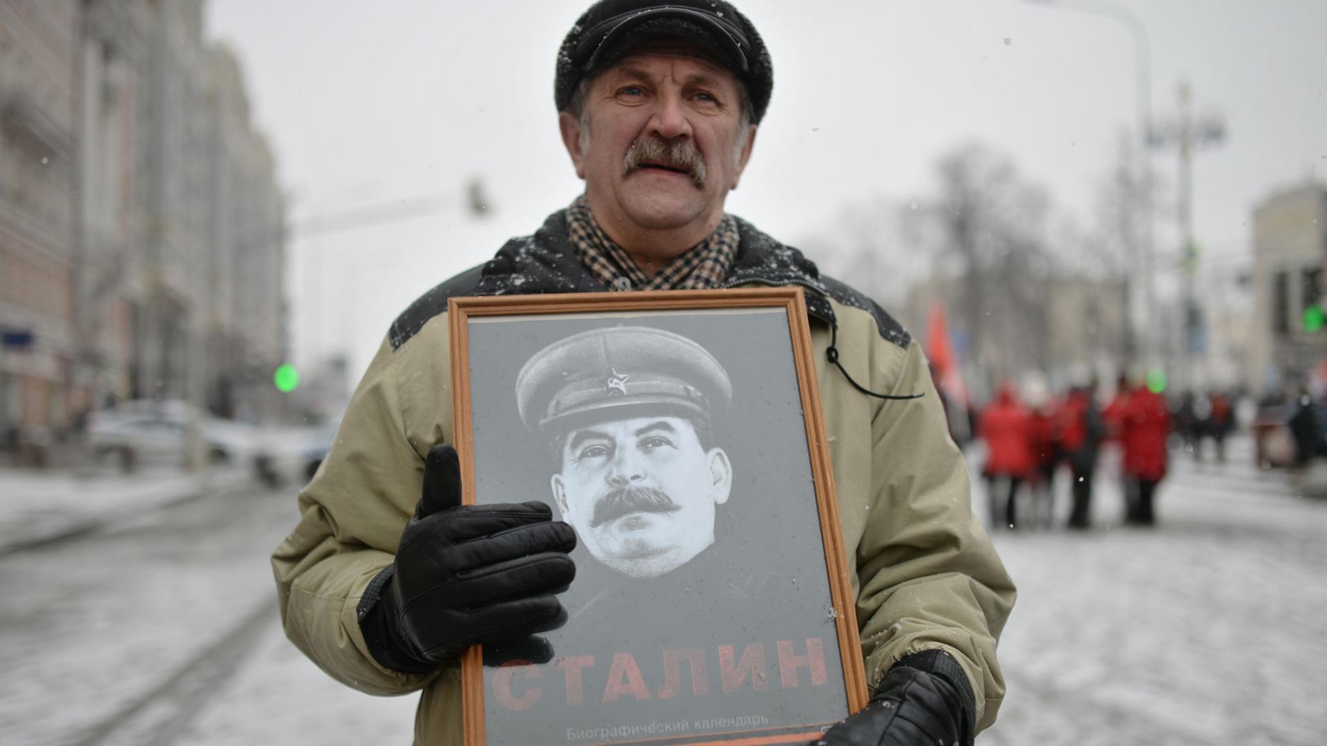 Ein Teilnehmer einer Prozession anlässlich des 99. Jahrestages der Entstehung der Sowjetarmee und der Marine hält ein gerahmtes Stalin-Bild in seinen Händen.