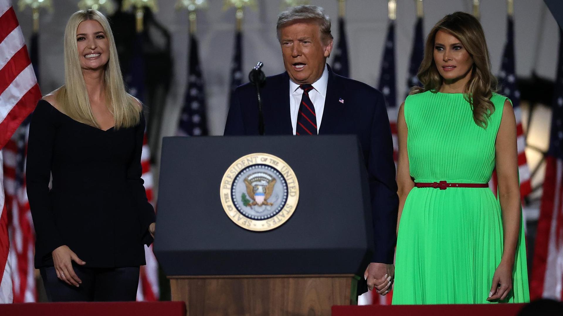 Präsident Trump an einem Rednerpult, mit seiner Frau Melania rechts und seiner Tochter Ivanka links von ihm.