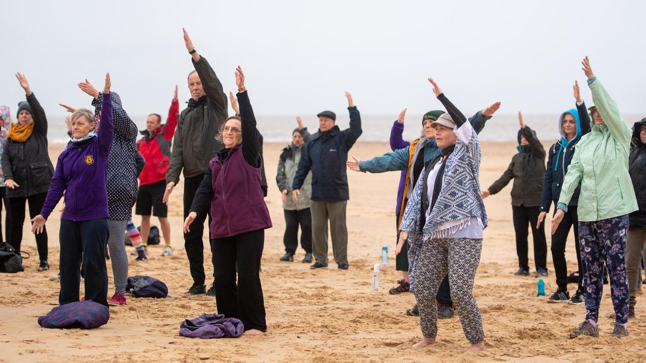 Ältere Menschen bei Meditations-, Konzentrations- und Bewegungsübungen am Strand.