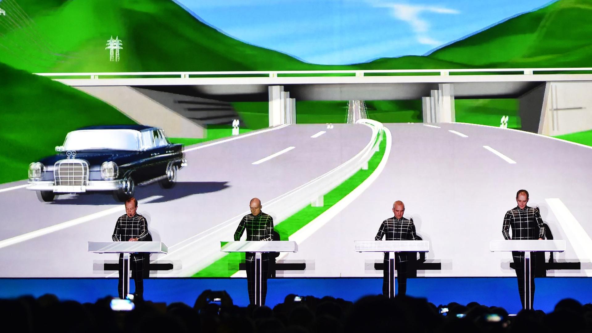 Die Band Kraftwerk spielt auf der Bühne, im Hintergrund ist eine riesige computeranimierte Leinwand zu sehen. 