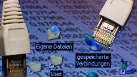 Netzwerkstecker sind vor einem Computer-Bildschirm mit Symbolen für "gespeicherte Verbindungen" zu sehen