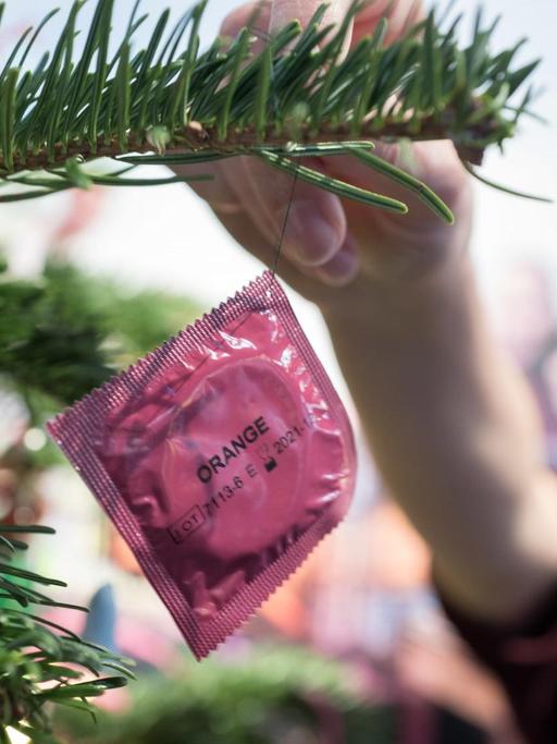 Eine Frau dekoriert einen Weihnachtsbaum mit einem Kondom.