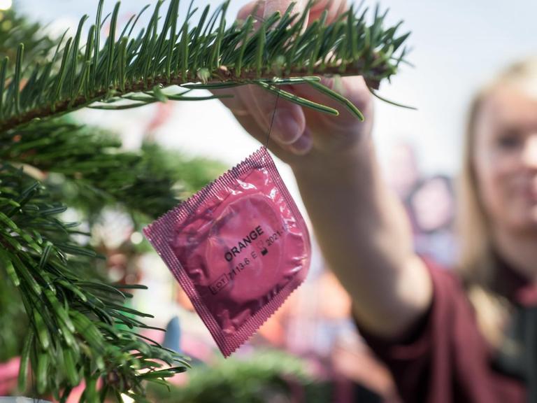 Eine Frau dekoriert einen Weihnachtsbaum mit einem Kondom.