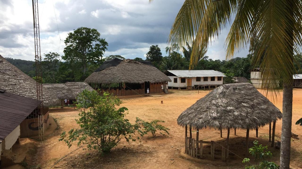 Ein Dorfzentrum im Dschungel mit Hütten aus Holz und Stroh.