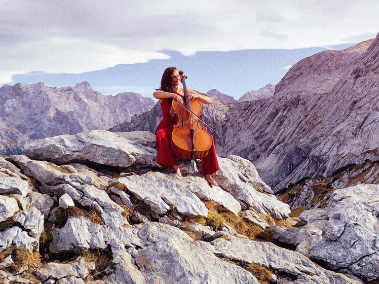 Raphaela Gromes sitzt mit ihrem Cello auf einem Felsen. Im Hintergrund ist ein Bergpanorama zu sehen