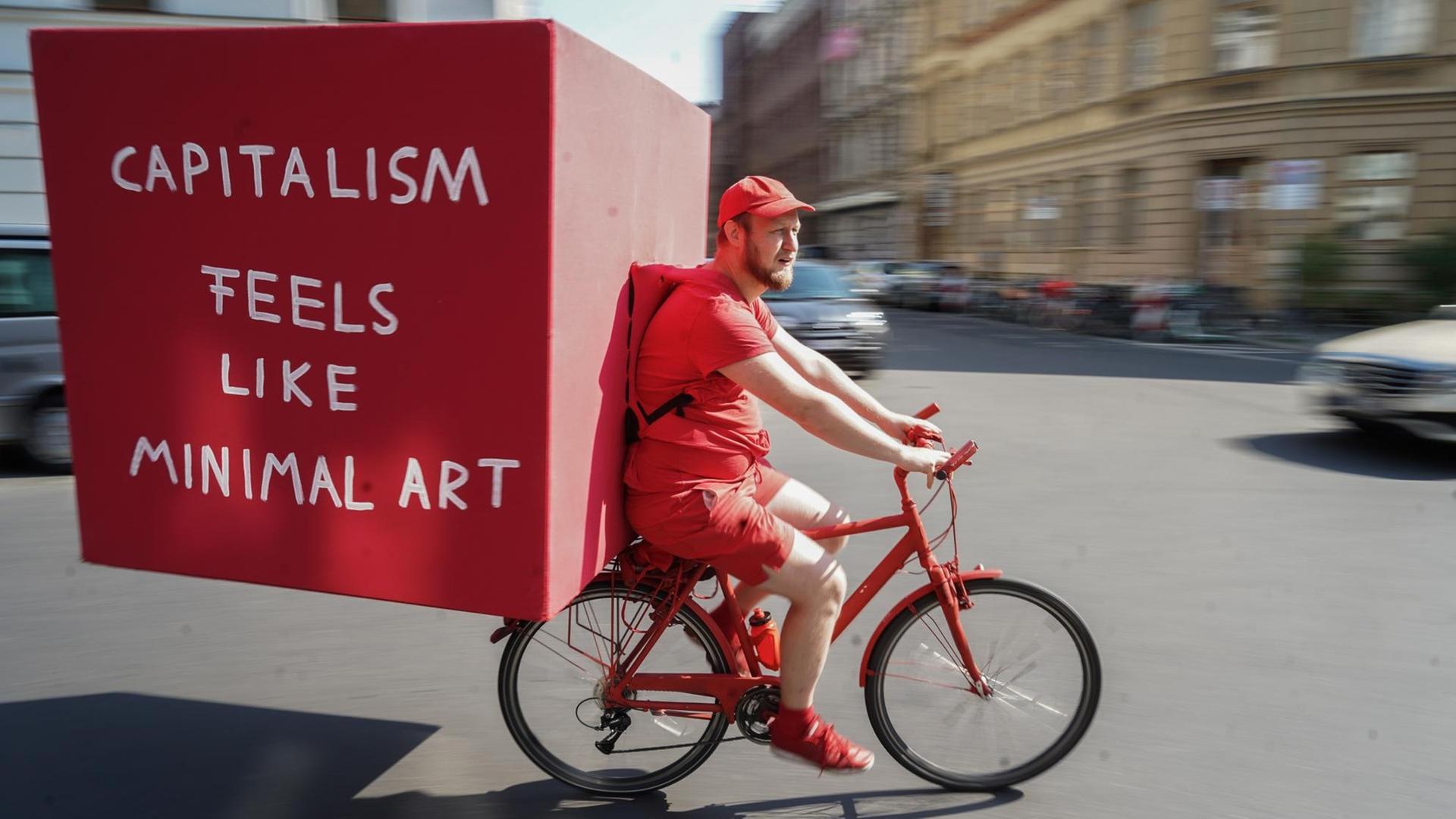 Im Rahmen der Berlin Art Week fährt der Künstler Daniel Chluba in roter Kleidung auf einem roten Fahrrad mit einer großen roten Kiste auf dem Rücken durch die Stadt.