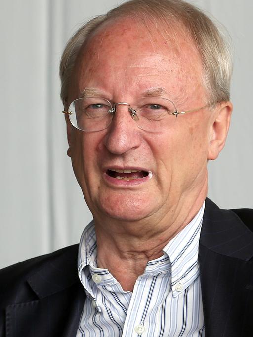 Klaus Staeck sitzt vor einem Mikrofon und hebt die Hand