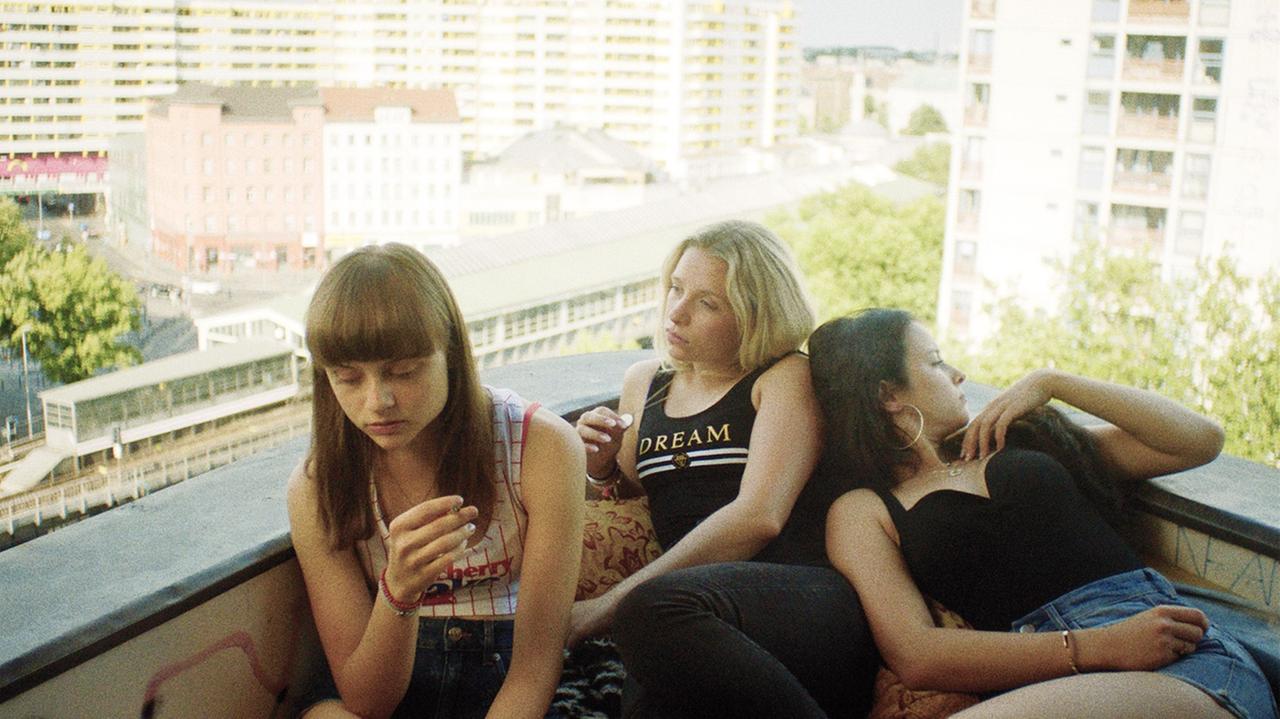 Im Still aus "Kokon" sitzen drei Mädchen im Sommer auf einem Dach in Berlin-Kreuzberg.