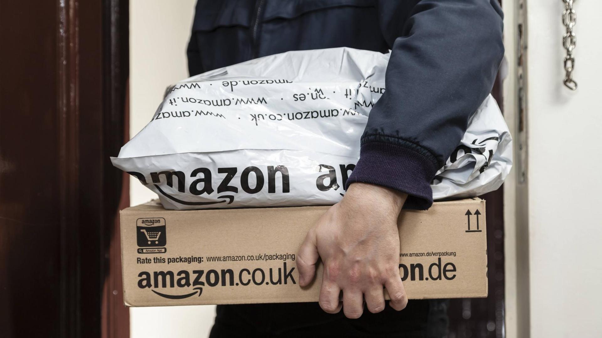 Ein Paketbote übergibt zwei Amazon-Pakete.