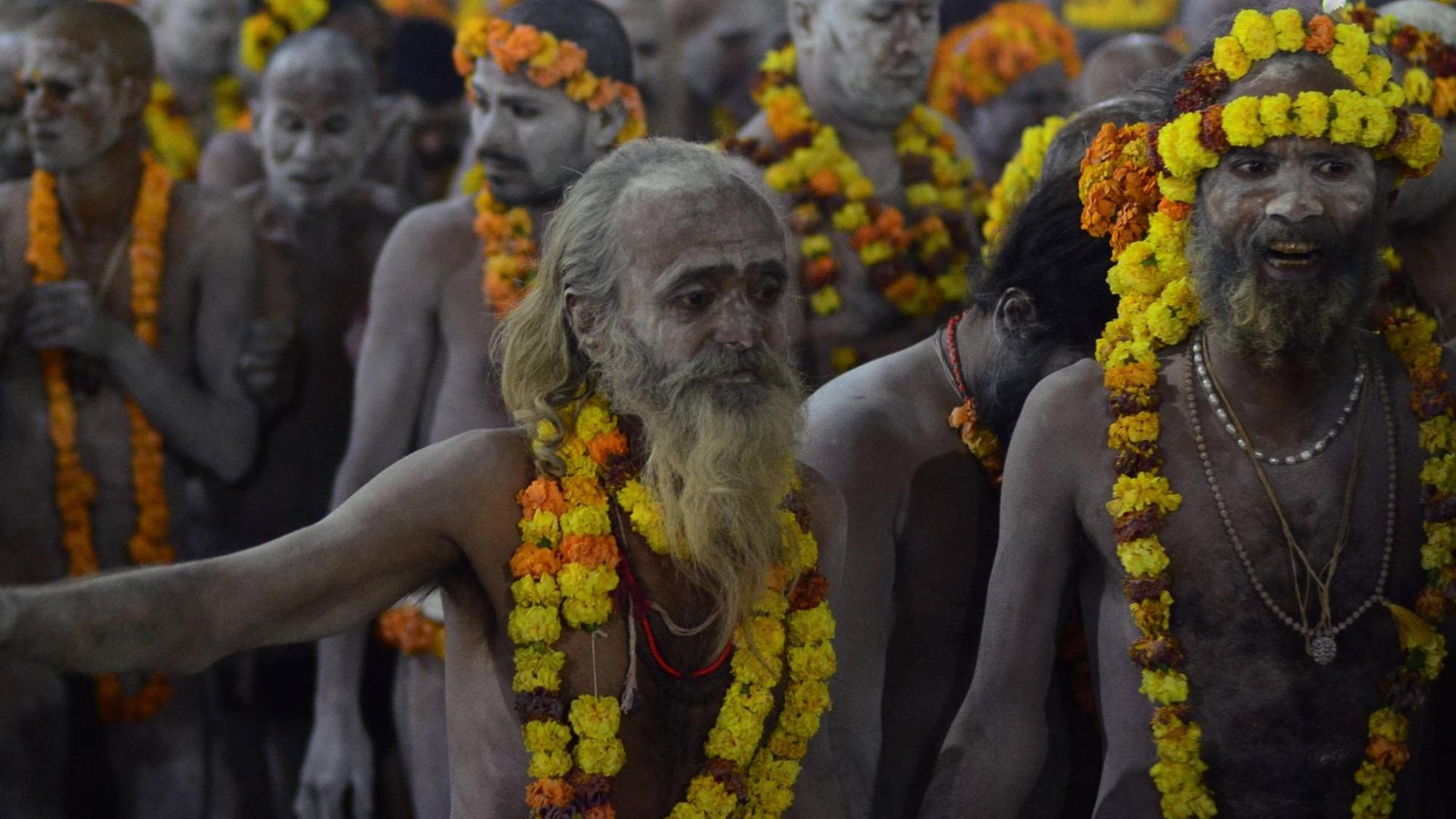Hindu-Pilgerfest Kumbha Mela: Nackte Männer mit Girlanden um Hals und Kopf auf dem Weg zum heiligen Bad im Ganges.