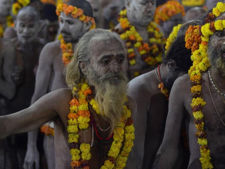 Hindu-Pilgerfest Kumbha Mela: Nackte Männer mit Girlanden um Hals und Kopf auf dem Weg zum heiligen Bad im Ganges.