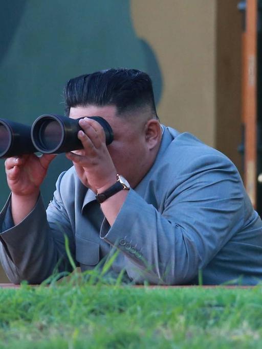 Nordkoreas Machthaber Kim Jong Un beobachtet mit einem Fernglas einen Raketentest.