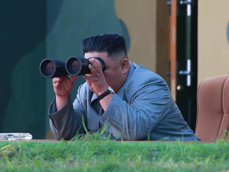 Nordkoreas Machthaber Kim Jong Un beobachtet mit einem Fernglas einen Raketentest.