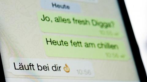 Ein fiktiver Dialog mit dem Satz "Läuft bei dir" ist auf einem Smartphone-Display in dem Messenger WhatsApp zu sehen.